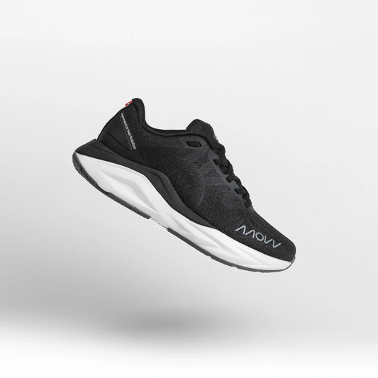 A black athletic running shoe with white midsole photographed against a light gray background. The shoe features a dark mesh upper material, black laces, and MOVV branding visible on the side.