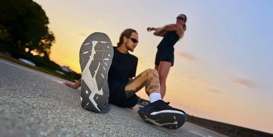 White and grey minimalist running shoe sole with injury reduction, man sitting and woman stretching outdoors