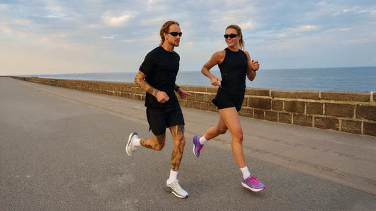 Two runners wearing best running shoes for pronated feet jogging together along coastal pathway during sunset