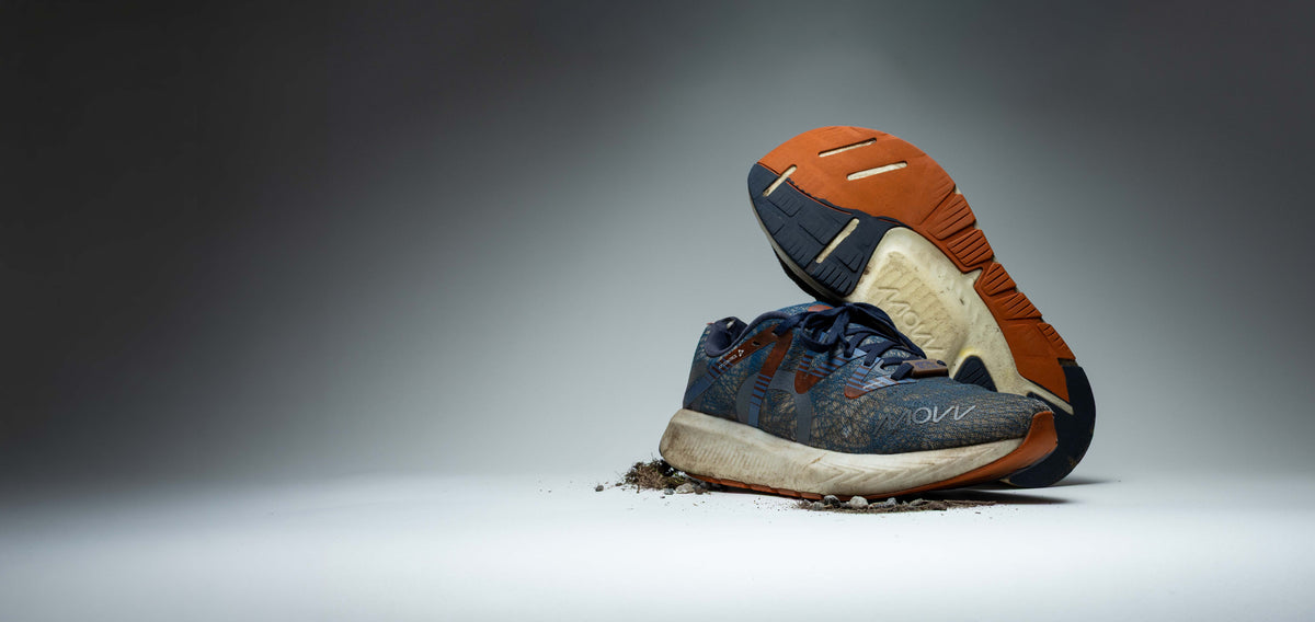 Pair of worn MOVV running shoes after 2,600 km, one resting on its side to show the heavily used orange outsole.