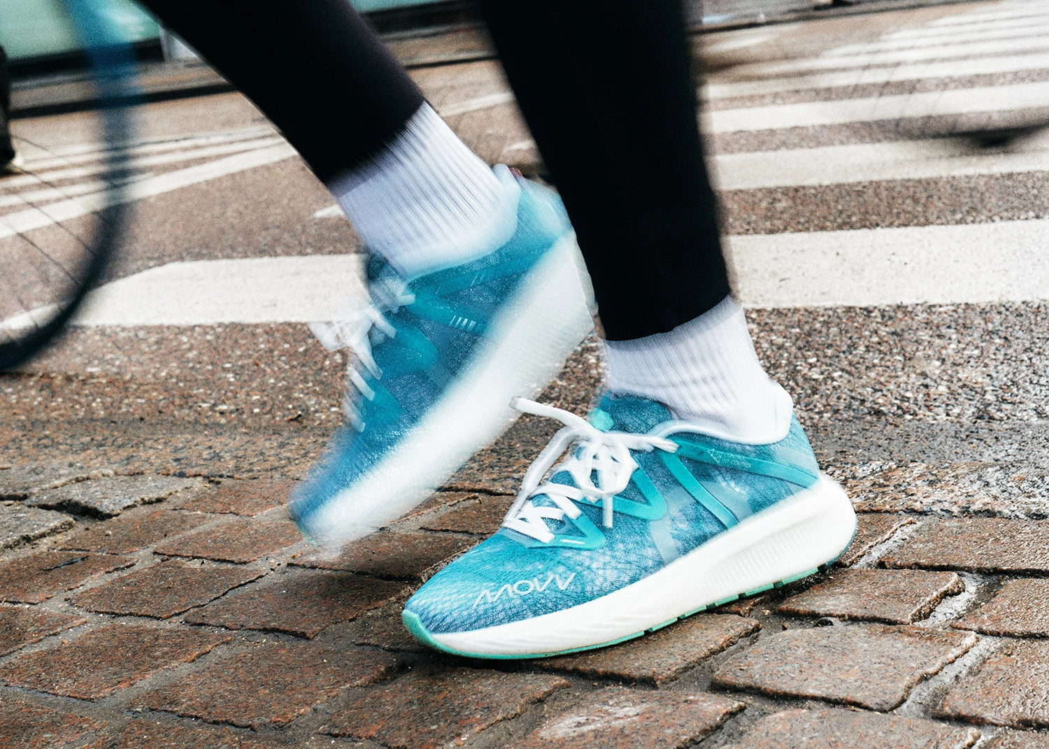 Person wearing blue MOVV running shoes with white laces on a brick pavement.