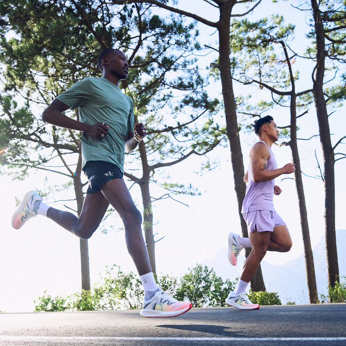Two male runners jogging on a scenic forest road at sunrise, wearing lightweight performance MOVV running shoes and activewear during an outdoor training run.