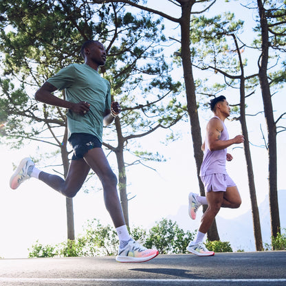 Two male runners jogging on a scenic forest road at sunrise, wearing lightweight performance MOVV running shoes and activewear during an outdoor training run.